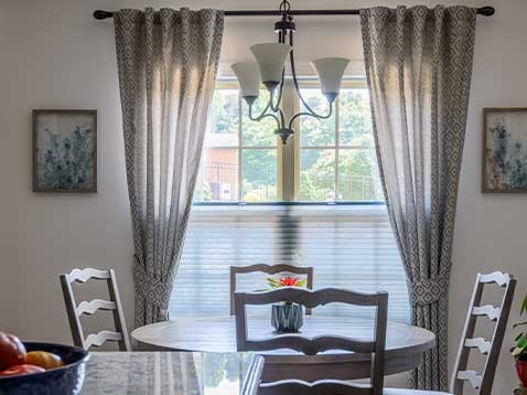 Four seats at a small round table, backed by a large window with drapery